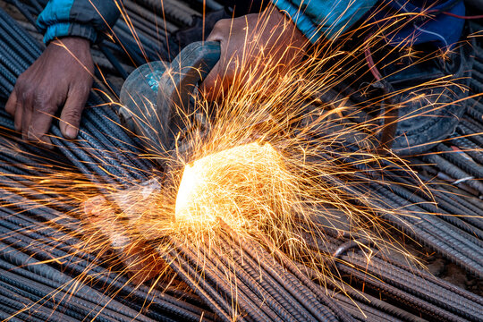 Closeup of a man cutting TMT Steel Bar with circular grinder used in construction.