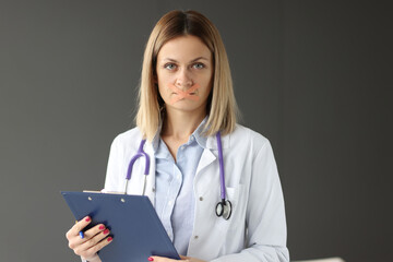 Doctor with clipboard in his hands and tape sealed over his mouth