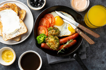 Breakfast in iron pan - fried eggs, sausages, tomatoes,broccoli, olives, toasted bread, coffee cup and juice glass. Top view breakfast food.