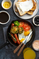 Breakfast in iron pan - fried eggs, sausages, tomatoes,broccoli, olives, toasted bread, coffee cup and juice glass. Top view breakfast food.