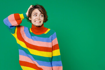 Preoccupied puzzled pensive young brunette woman 20s years old wearing basic casual colorful sweater stand put hand on head looking aside isolated on bright green color background studio portrait.