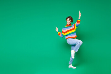 Full length side view of cheerful funny young brunette woman 20s in casual colorful sweater dancing pointing index fingers up winner gesture isolated on bright green color background studio portrait. - obrazy, fototapety, plakaty