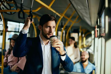 Male entrepreneur having takeaway coffee while commuting to work by bus.