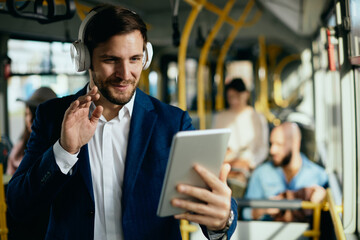 Happy businessman having video call over touchpad in a public transport.