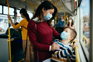 Happy mother and son talking while commuting by bus and wearing protective face masks.