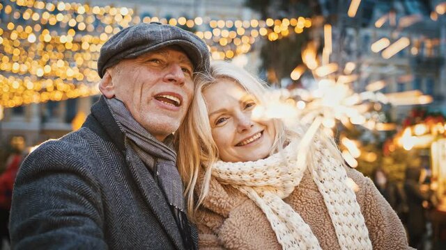 Close up portrait of happy senior man and woman embracing in city center, holding bengal lights, tracking shot