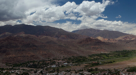 Bucolic landscape. Panorama view of the village Tilcara at the foot of Humahuaca ravine. The brown Andes mountains, green valley, arid desert and buildings under a beautiful sky. 