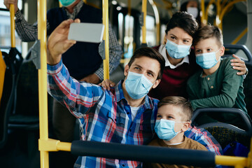 Obraz premium Happy family with face masks taking selfie while commuting by bus.