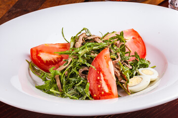 Beef tongue salad with arugula, tomatoes and quail egg on white plate