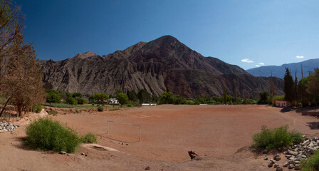 Love for sports. Panorama view of an empty football field in the desert. The rustic soccer goals, sand ground and surrounding mountains in a hot day in Purmamarca, Jujuy, Argentina.  