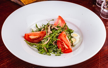 Beef tongue salad with arugula, tomatoes and quail egg on white plate