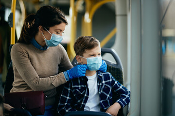 Small boy and his mother wearing face masks while commuting by bus during coronavirus pandemic.