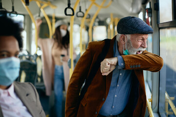 Senior man coughing into elbow while commuting by bus.