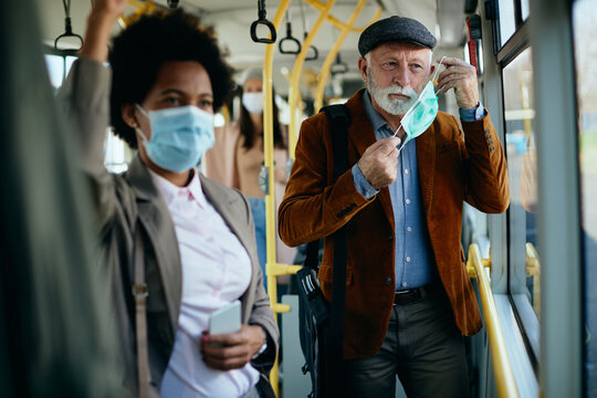 Mature man putting on protective face mask in a public transport.