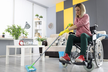 Woman in wheelchair washes the floor with mop