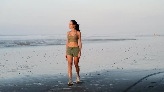 athletic girl in shorts and a tank top walks along the beach after a workout USA