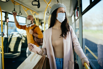 Woman with shopping bags wearing face mask while commuting by bus.
