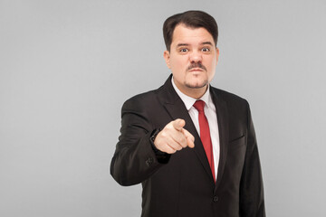 Boss have bad mood. I warn you the last time, I'm seriously! indoor studio shot. isolated on gray background. handsome businessman with black suit, red tie and mustache pointing and looking at camera