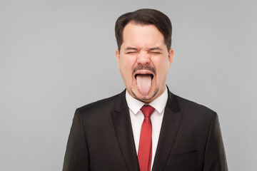 Closeup portrait of crazy man in classic suit, tongue out, and roar. indoor studio shot. isolated on gray background. handsome businessman with black suit, red tie and mustache with closed eyes