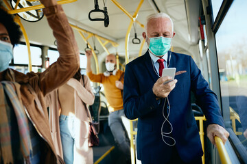 Senior businessman with face mask using smart phone in a public transport.
