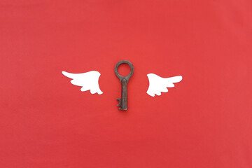 Two wings are white, the key is made of iron subject to corrosion on a red background.