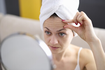 Woman examines her forehead wrinkles in mirror