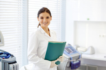female doctor with document case in hands and looking at camera, posing, at work place. portrait