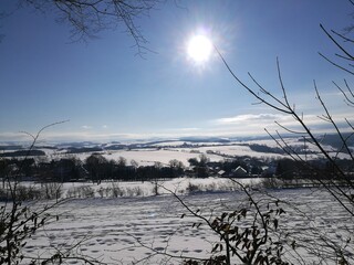 Skispuren in einer Winterlandschaft; hügelige Landschaft im Erzgebirge in Sachsen, verschneite Dörfer, Wintersonne am blauen Himmel, 