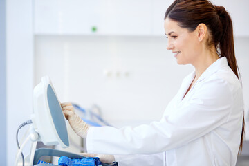 female doctor push buttons on medical equipment, enjoys working in hospital. use modern equipments for treatment in clinic. medicine and healthcare concept. side view