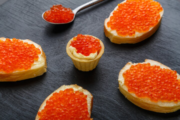 Naklejka na ściany i meble Canapes with butter and red caviar on a black board on a concrete background.