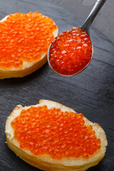 Toast with butter and red caviar and a spoon with caviar on a black board.