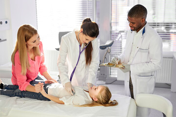 Obraz premium nice pediatricians working with children patients, check the health of kid girl came with mom. african and caucasian medical workers in clinic