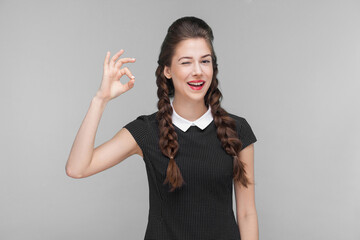 Gesture woman toothy smile and showing ok sign at camera. Indoor, studio shot isolated on gray background