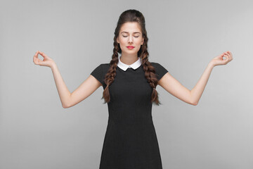 Meditating, zen practice. Young woman doing yoga. Indoor, studio shot isolated on gray background
