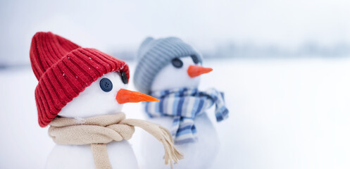 Holiday card with snowmen, banner. Two little cute snowmen in hats and scarves on the snow on a winter day, close-up. 