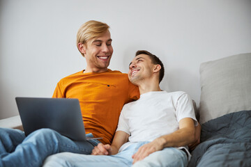 Happy gay couple cuddling and using laptop at home