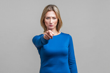 Hey you! Portrait of serious bossy woman in tight blue dress pointing at camera frowning with...
