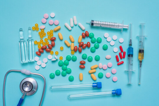 Various medical tablets and pills, syringe, stethoscope,  laboratory flask and ampoules on the blue background.