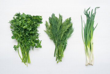 Green branches of parsley, dill and green onions on the white flat lay background.