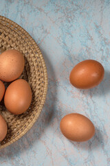 several fresh chicken eggs in a straw basket on a wooden background. Healthy eating concept.