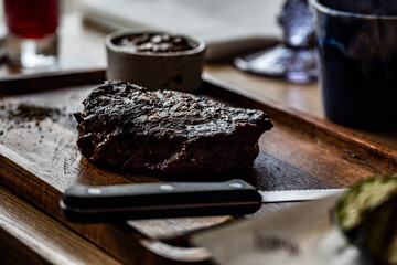 still life with a large piece of grilled meat on a wooden plate