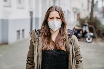 Portrait of happy young woman in winter with thick clothes walking down the street wearing medical...