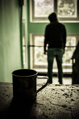 a metal mug stands on a concrete staircase stands, in the background a homeless man