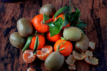 Clementines with leaves and kiwi fruit on an old wooden table