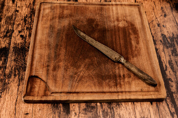 Worn wooden cutting board on an old worn wooden table with an old knife on it