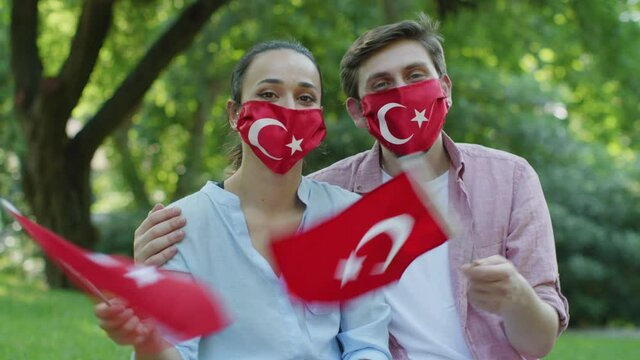 Two young people are waving the Turkish flag while looking at the camera.	They wear a medical mask in the form of a Turkish flag to protect them from the virus