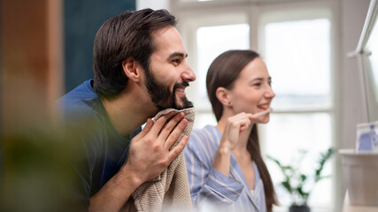 Young couple brushing teeth in front of mirror indoors at home.