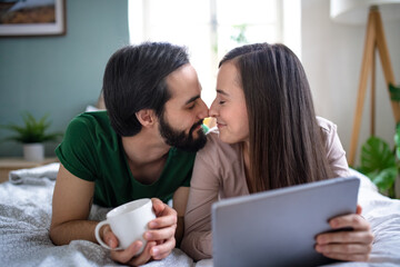 Young couple in love using tablet on bed indoors at home.