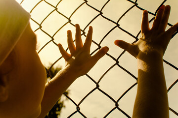 The child's hands are stretched out to the metal mesh.