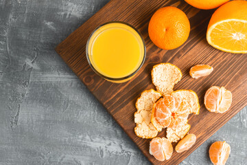 Fototapeta na wymiar Glass of fresh orange juice, whole and sliced fruits on wooden board, top view with copy-space